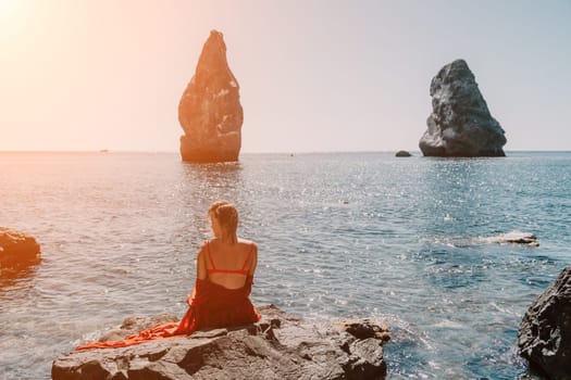 Woman travel sea. Young Happy woman in a long red dress posing on a beach near the sea on background of volcanic rocks, like in Iceland, sharing travel adventure journey