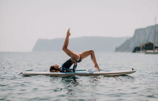 Woman sup yoga. Middle age sporty woman practising yoga pilates on paddle sup surfboard. Female stretching doing workout on sea water. Modern individual hipster outdoor summer sport activity