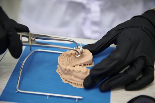 Close up. Selective focus on gypsum cast of human jaw. Dentist with black surgical gloves works on dental implant in medical lab. Prosthetic engineer at work. Extreme precision. Dentistry. Copy space