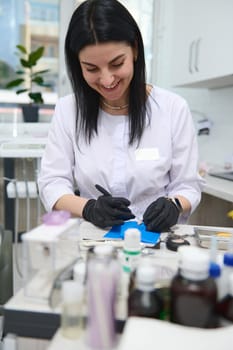 Portrait of a positive smiling female dentist doctor, prosthetic engineer working with gypsum cast of human jaw, preparing dental prosthetic, implants in medical laboratory of dentistry clinic