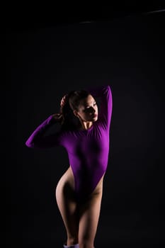 Attractive and slender brunette girl in a violet bodysuit underwear in studio. Body care concept.