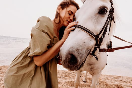 A woman in a dress stands next to a white horse on a beach, with the blue sky and sea in the background