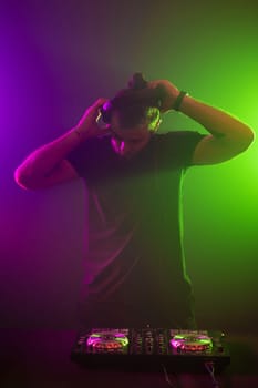 Handsome DJ in a black T-shirt at work mixing sound on her decks at a party or night club with colourful smoke light background