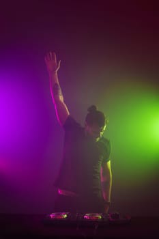 Handsome DJ in a black T-shirt at work mixing sound on her decks at a party or night club with colourful smoke light background