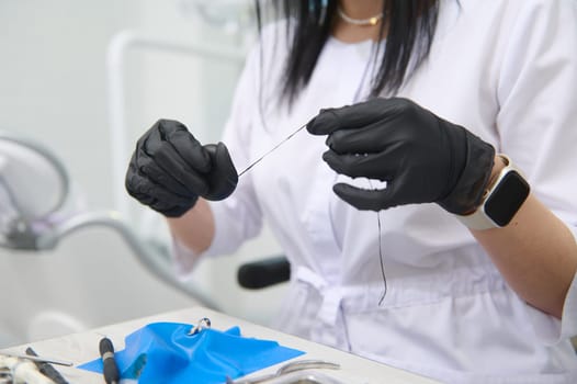 Close-up dental floss in the hands of a doctor dentist wearing black surgical gloves, working with gypsum dental model of human jaw in medical clinic. Dental health and oral hygiene concept. Dentistry