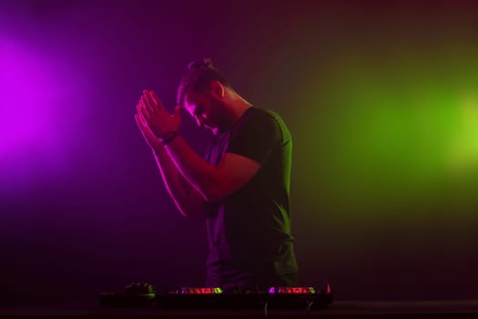 Handsome DJ in a black T-shirt at work mixing sound on her decks at a party or night club with colourful smoke light background