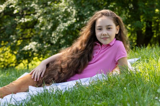 Little Adorable Girl With Extra Long Hair Lying On Grass in Meadow. Caucasian Asian Brown Haired Child Having Fun, Enjoying Nature. Carefree, Happy Childhood, Closeup, Horizontal Plane