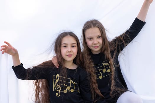 Two Smiling Girls, Sisters With Long Hair Having Fun Under Sheet On Grass in Park, Making Tent. Caucasian Asian Siblings Enjoy Time Together. Carefree Childhood, True Friendship. Horizontal Plane