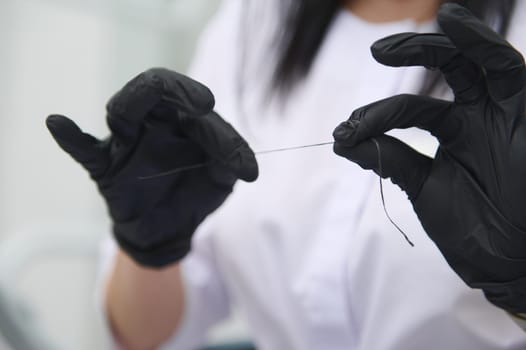 Close-up dental floss in the hands of a doctor dentist, dental hygienist wearing black surgical gloves. The concept of dental health and oral hygiene. Dentistry. Hygiene. Healthcare and medicine