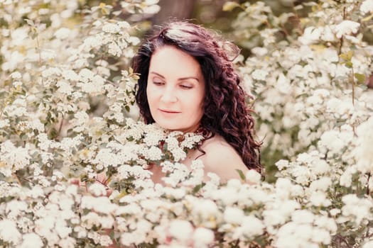 Woman spirea flowers. Portrait of a curly happy woman in a flowering bush with white spirea flowers