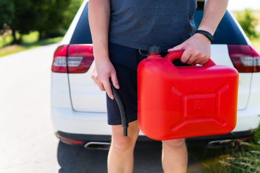 A man holds a red canister near a white car, close-up. Stop to refuel, no refueling, fuel problems