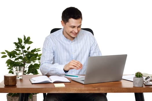 young friendly businessman talking at laptop webcam, sitting on chair at desk, using laptop