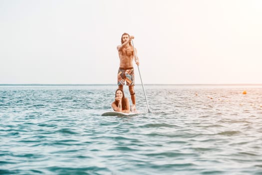 Silhouette of woman standing, surfing on SUP board, confident paddling through water surface. Idyllic sunset or sunrise. Sports active lifestyle at sea or river.