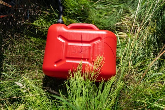 Red plastic canister among the green grass near the white car. Problems on the road with fuel for the car, refueling on the road, self-refueling