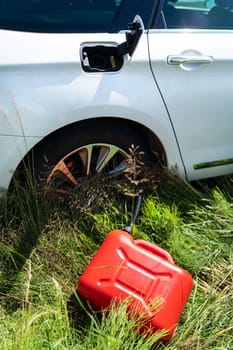 Red plastic canister among the green grass near the white car. Problems on the road with fuel for the car. Vertical photo