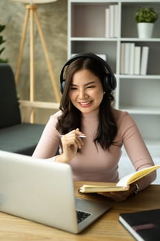 Smiling young woman wearing headphone learning distantly, watching online lecture on laptop at home.