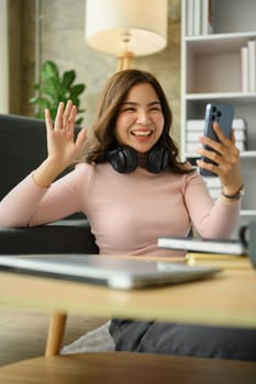 Smiling asian woman waving hand, having video calling on smartphone. People, technology and communicating.