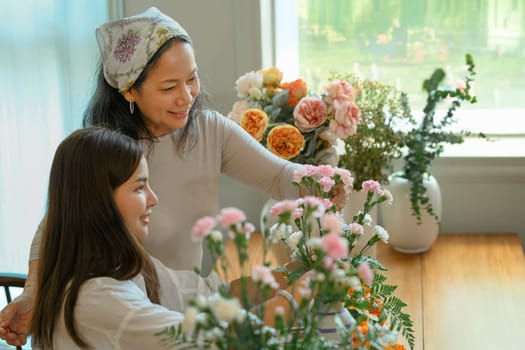 Moment of senior woman and adult daughter creating beautiful bouquet with different flowers at floral shop. Small business concept.