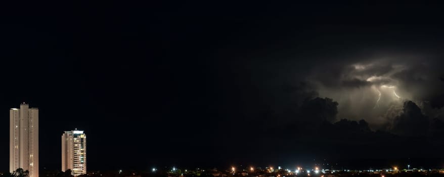 Two skyscrapers rise above the city in a majestic manner during a dark night with thunder and lightning in the background. Space for text available.