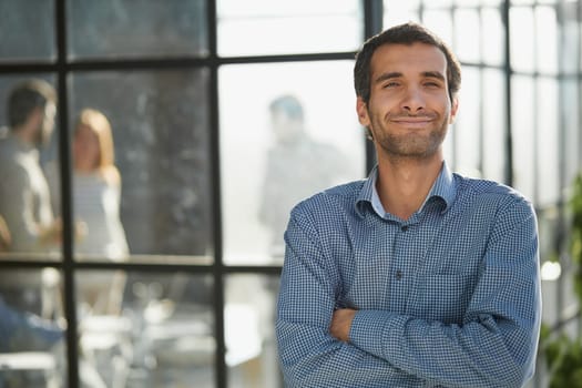 Middle aged white male creative in casual office lounge area looking to camera, arms crossed, waist up