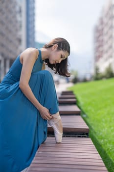 Beautiful asian ballerina in blue dress adjusting her pointe shoes outdoors