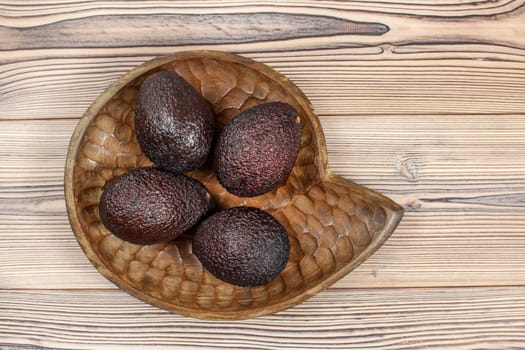 Top down view, four ripe avocados in wooden carved bowl, on wooden desk.