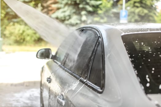 Side window of car washed in self serve carwash, high pressure jet water spraying on glass.