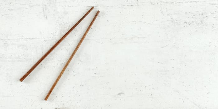 Top down view - pair of dark wood chopsticks on white board. Can be used as banner for asian / chinese food, space for text on right.