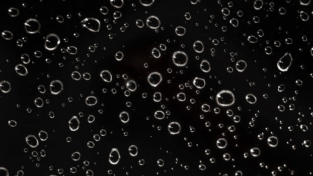 Closeup - rain water drops behind glass look like bubbles in black liquid. Abstract wet background.