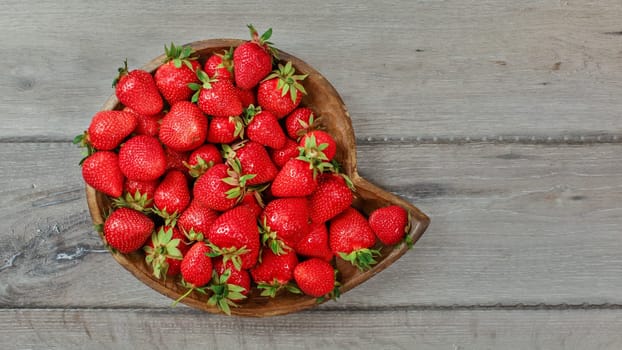 Top down view, strawberries in wooden carved bowl on gray wood desk.