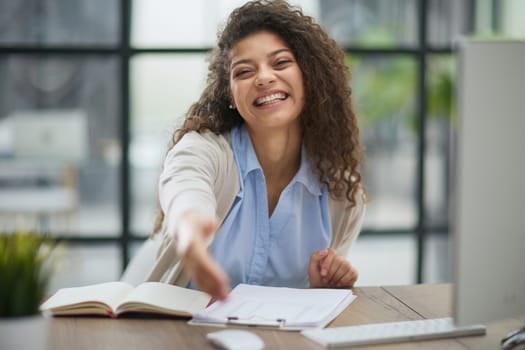 Happy young woman looking at the camera while welcoming a client. Smiling female executive manager, secretary offering professional business services