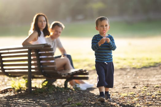 Cute little boy blowing soap bubbles with his parents behind his back looking for him. Mid shot