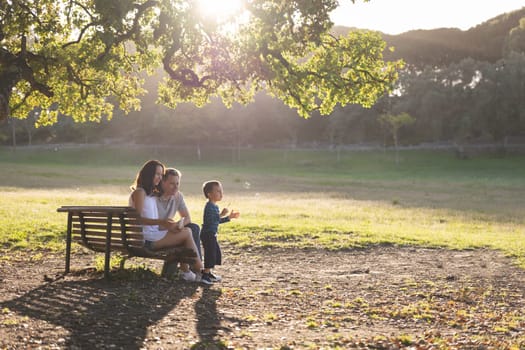 Cute white family spending time in the park - a little boy blowing soap bubbles while his parents sitting on a bench. Mid shot