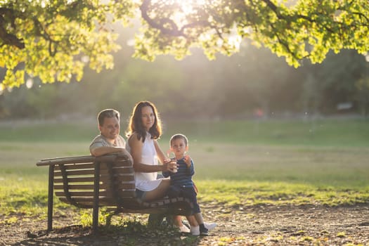 Cute family spending time in the park - sitting on a bench under the tree and looking in the camera. Mid shot