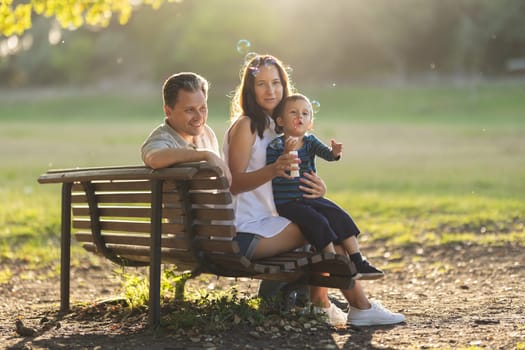 Cute white family sitting on a bench in the park. Mid shot
