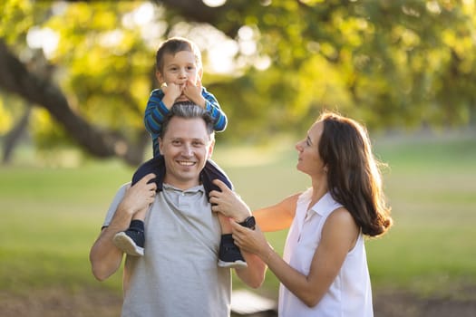 Cute white family in the park - little son on the shoulders of his father. Mid shot