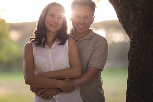 Adult smiling white couple hugging on nature. Mid shot