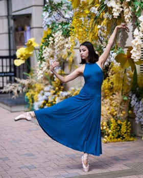 Beautiful Asian ballerina posing against the backdrop of a building decorated with flowers