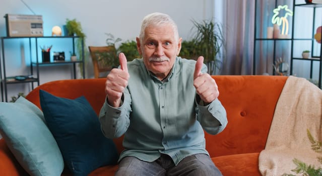 Like. Happy excited senior grandfather man looking approvingly at camera showing thumbs up, like sign positive something, good great news, positive feedback. Elderly guy sitting on couch at home room