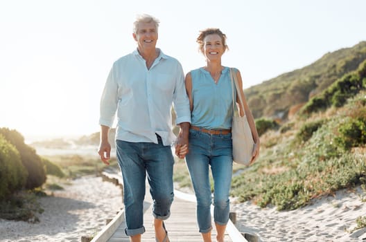 Senior, couple and walking at the beach with hands in portrait for happiness on a vacation in the outdoor. Mature, woman and man holding by ocean for travel on holiday with sunshine for the weekend