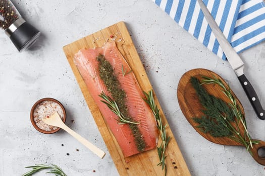 Salted fish fillet with spices and herbs: dill and rosemary on a wooden board on a gray background.