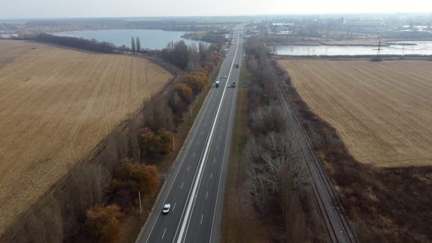 Large plowed field with plowed land and yellow dry straw after harvesting wheat, a lake, a highway with driving cars on an autumn day. Agro industrial agricultural farm landscape. Aerial drone view.