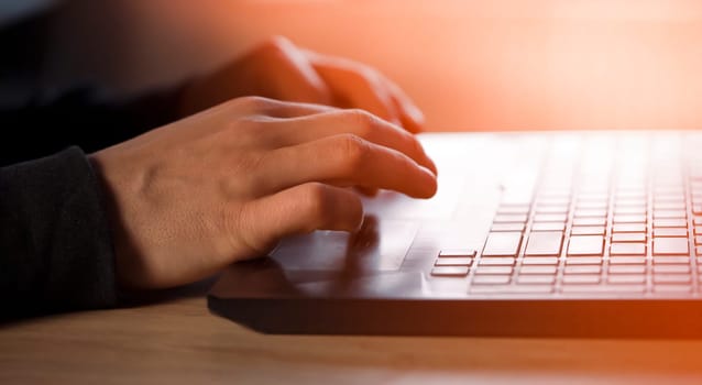 Male hands with a sun effect are typing on a laptop keyboard, close-up view. A man works in an office, is engaged in the development of his business at home, writes messages online.