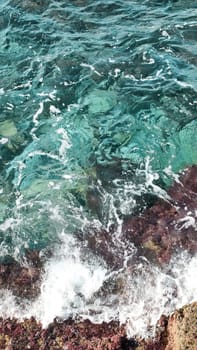Turquoise sea water, white foam and part of shore, top view, vertical frame