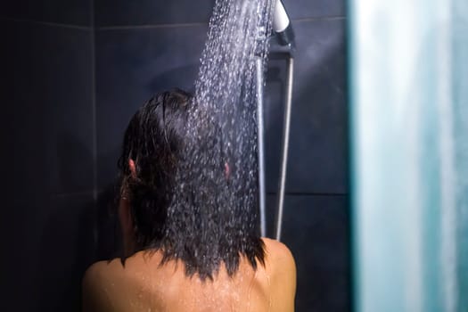 A young girl takes a shower with shampoo and soap, washes her hair, takes care of her body, hygiene and cleanliness in a modern gray shower room.