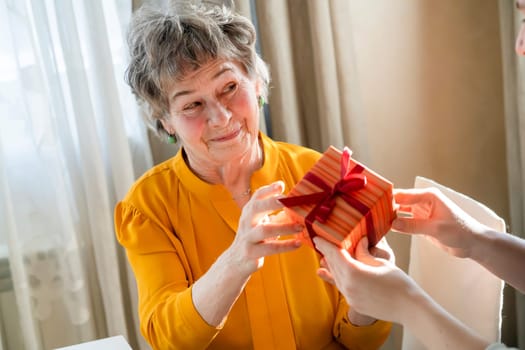 A young girl congratulates an elderly woman, her mother or grandmother, daughter holds in her hands a small cute beautifully wrapped gift for her grandparent, gives a surprise with love and care.