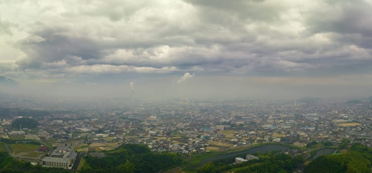 Panoramic aerial view of hazy city with smokestacks under cloudy sky. High quality photo