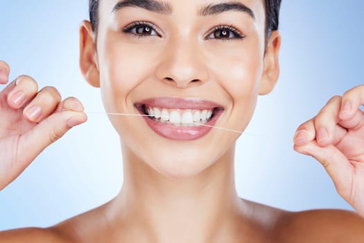 Face, flossing teeth and dental with woman, hygiene and beauty with grooming and mouth care on blue background. Hands, string and healthy gums with fresh breath, health and skin glow in portrait.