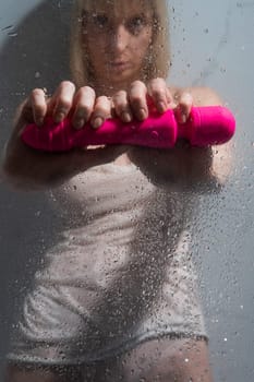 A woman in a white tank top stands in the shower and holds a pink sex toy