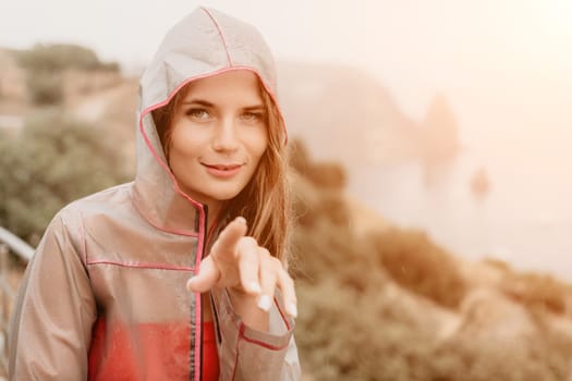 Woman rain park. Happy woman portrait wearing a raincoat with transparent umbrella outdoors on rainy day in park near sea. Girl on the nature on rainy overcast day